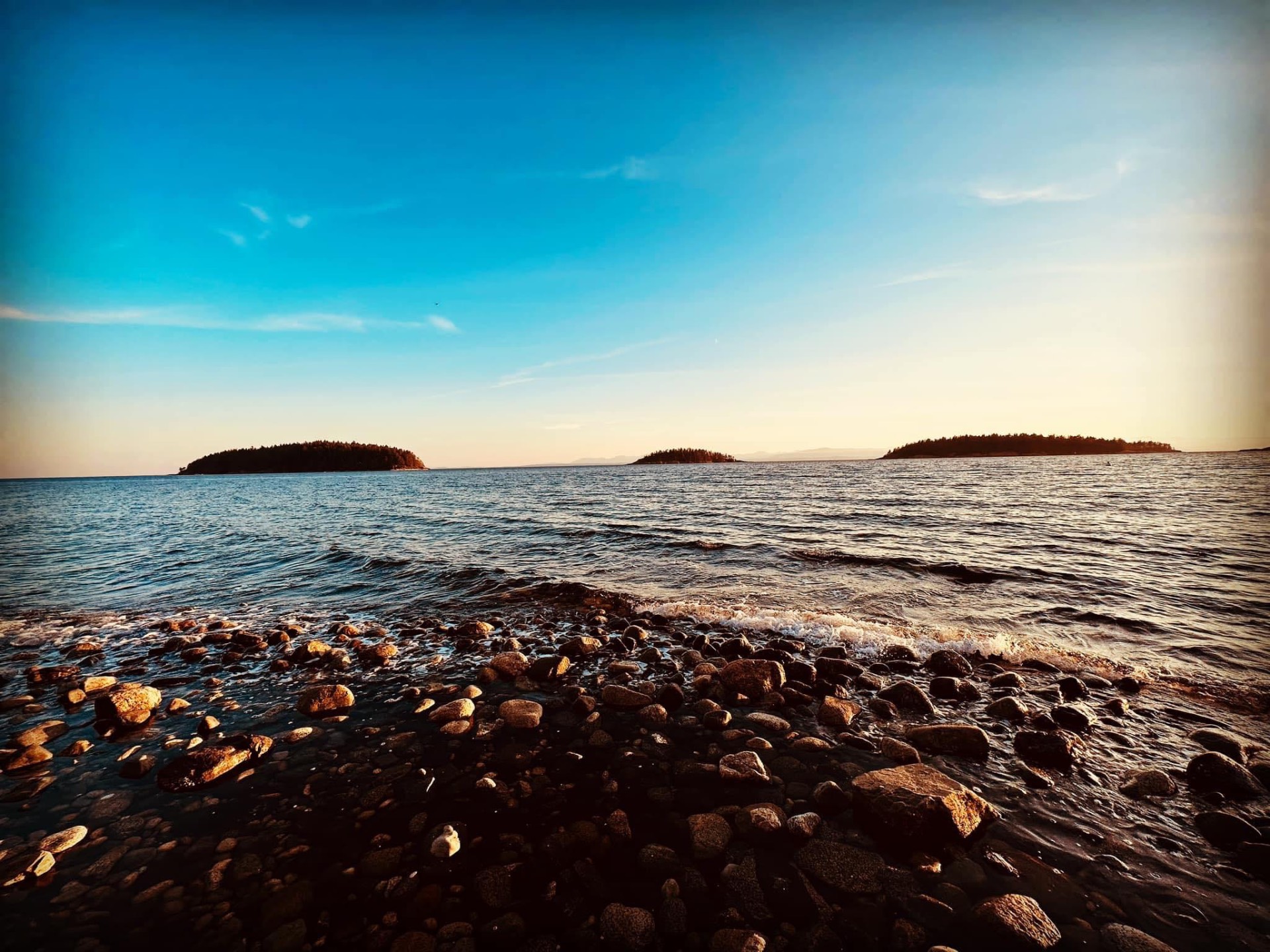 Three small forested islands on a calm sea at sunset